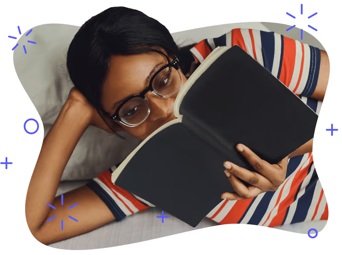 A college student reading a book while relaxing on a bed
